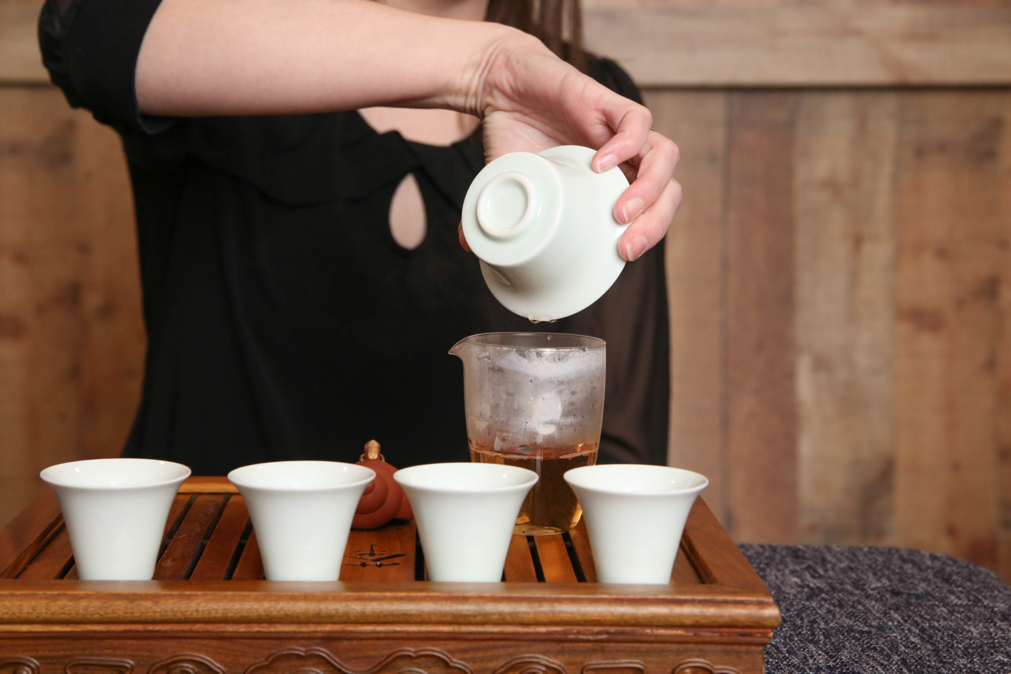 The Right Way to Make Tea - Woman in a black shirt pouring tea from a white gaiwan into a glass sharing pitcher.