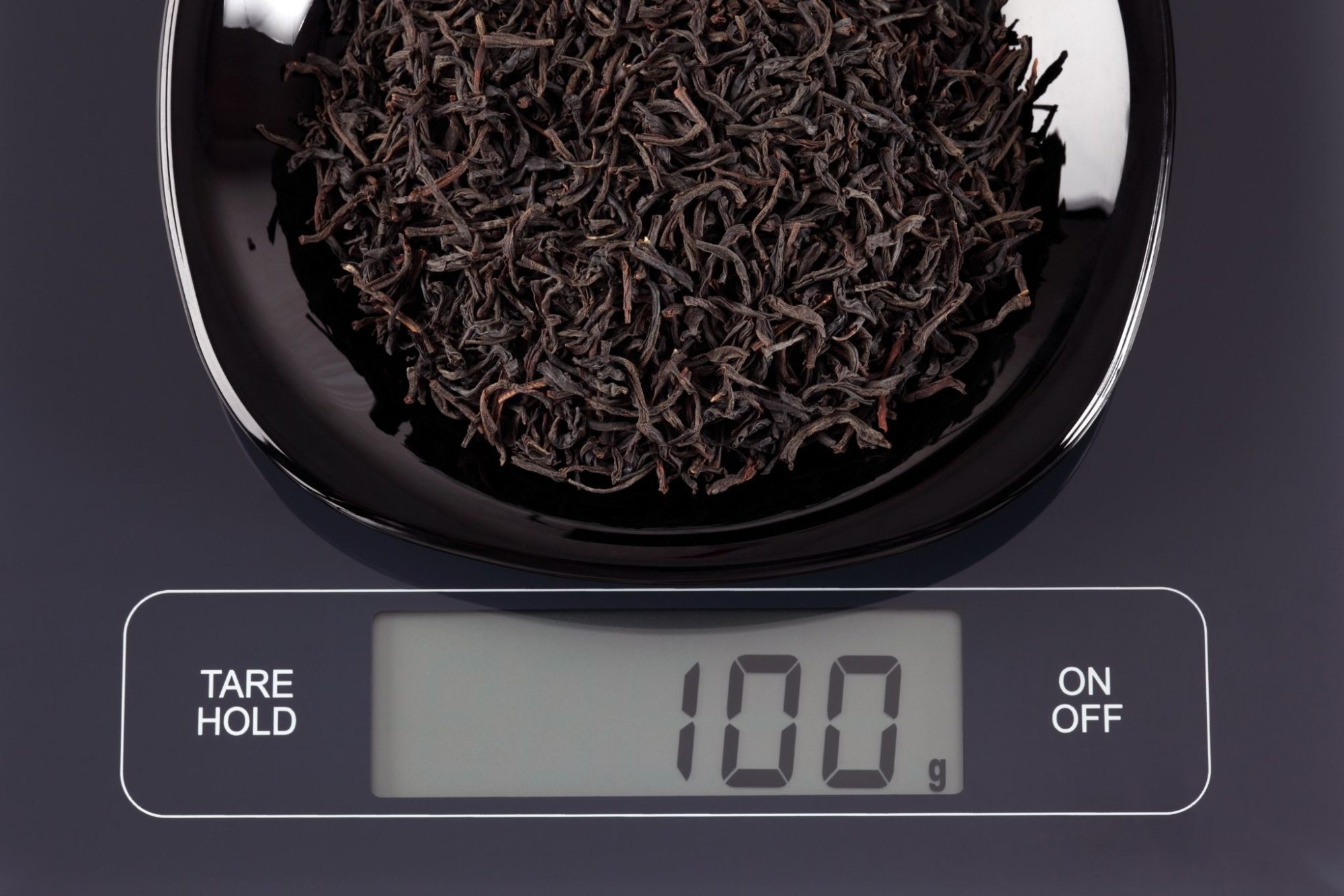 Get Started Drinking Tea - black tea leaves on a black digital scale. The display reads 100g.