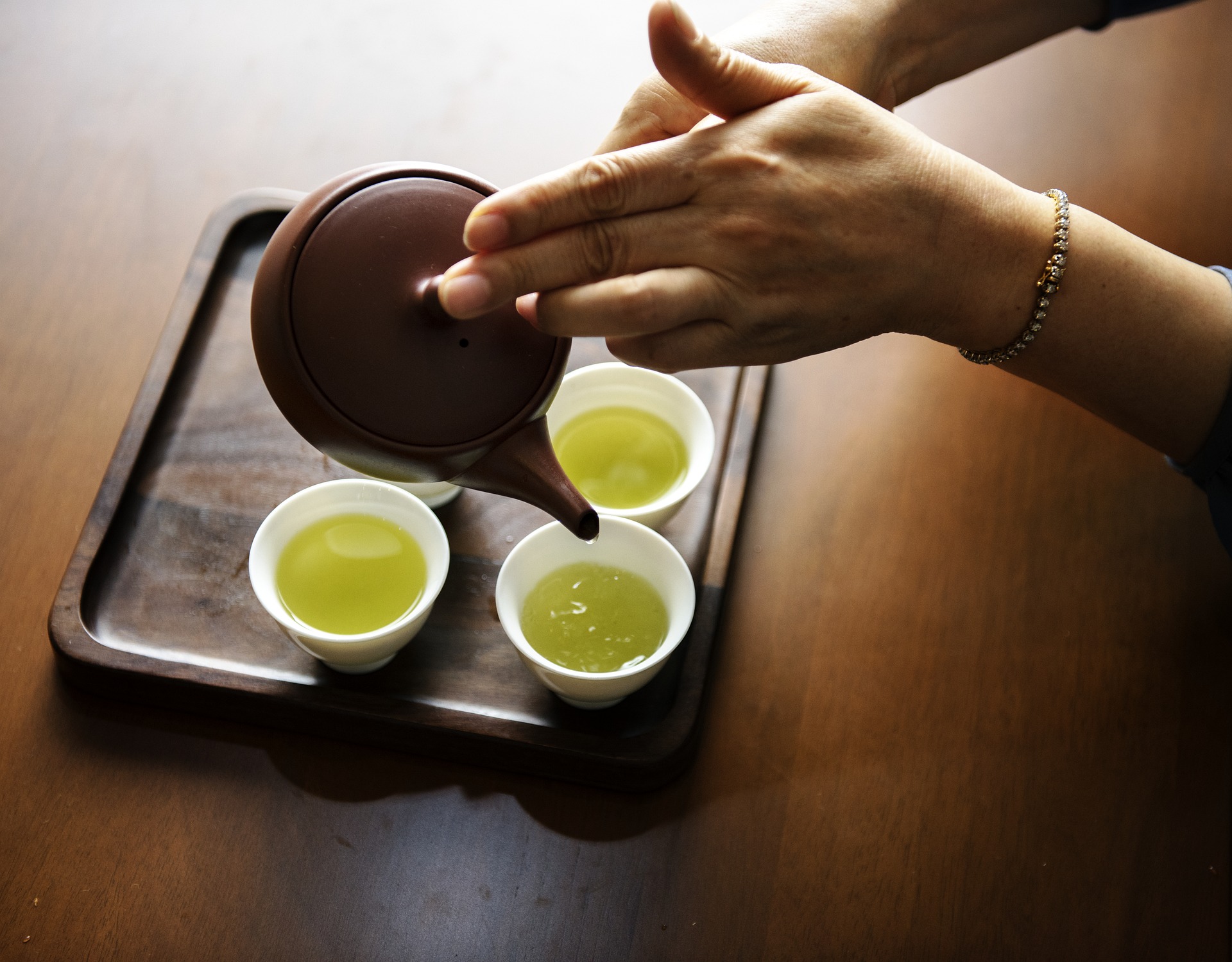 Get Started Drinking Tea - A brown kyusu teapot held by two hands is pouring green tea into a group of four white teacups