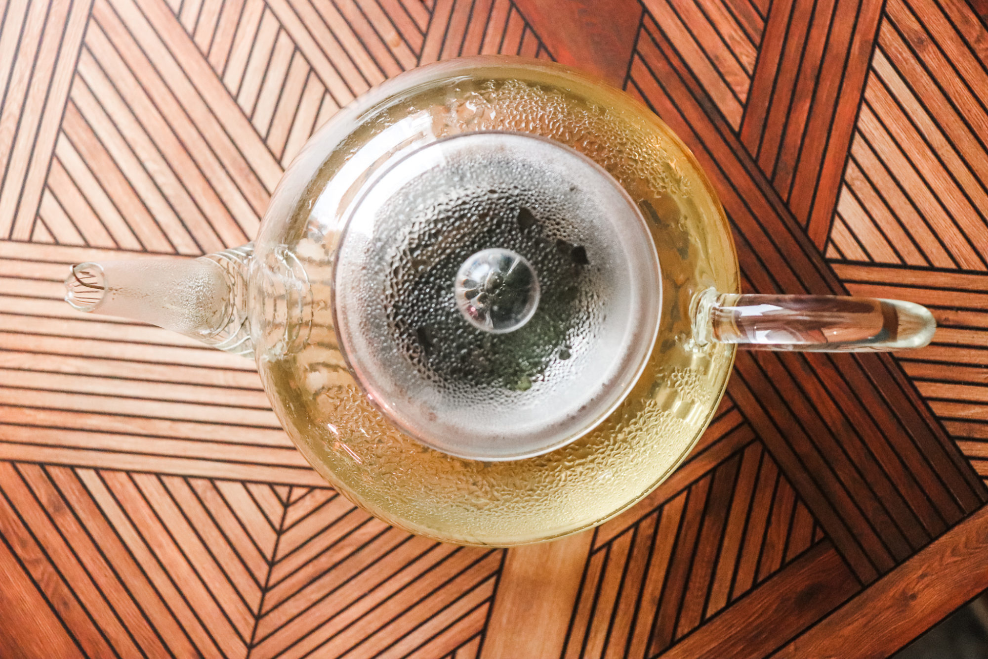 DAVIDsTea Organic Korean Sejak is brewed in a clear glass teapot on a parquet wood background.