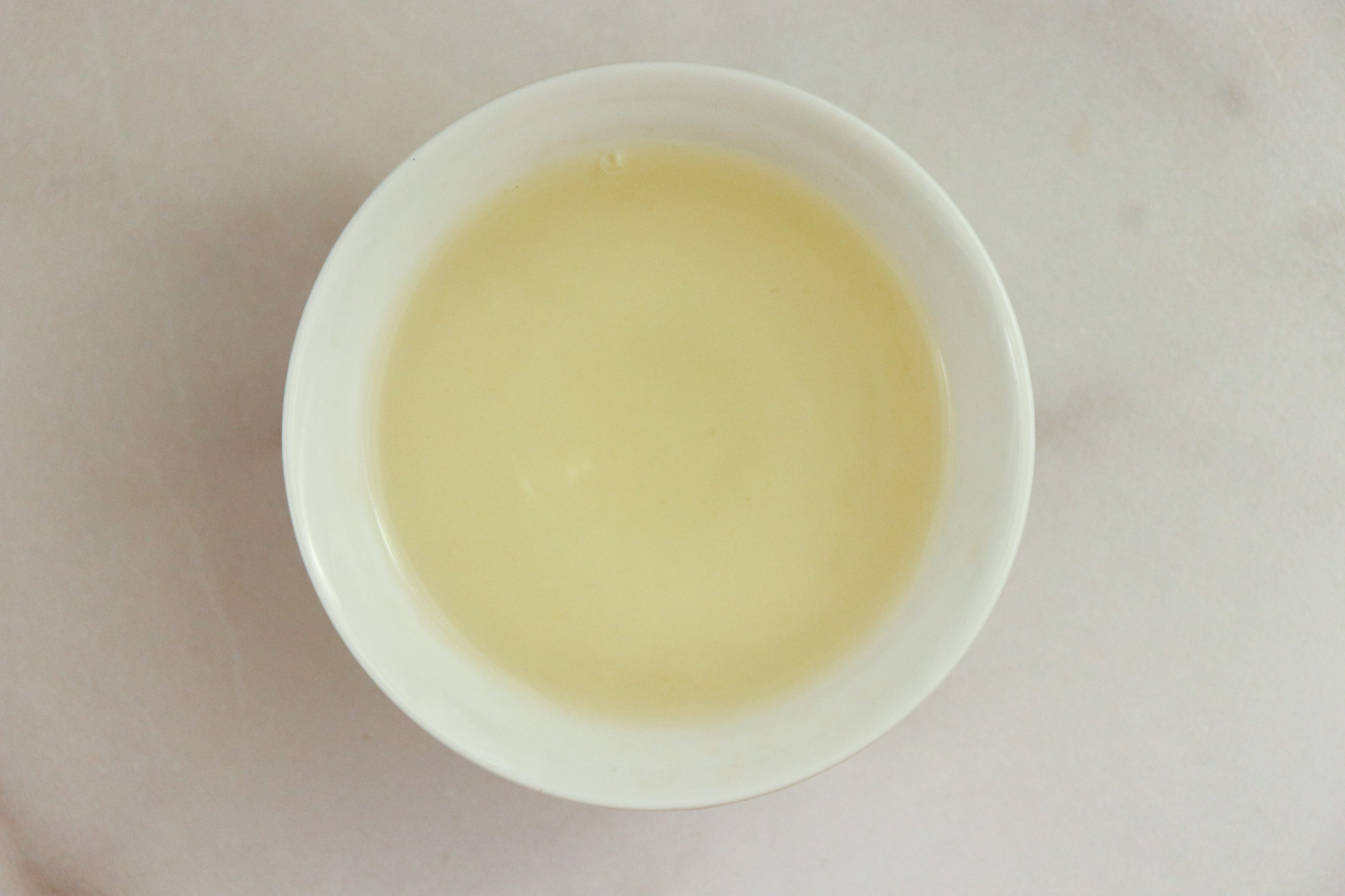 Huang Shan Mao Feng - pale yellow tea in a white teacup against a white marble background