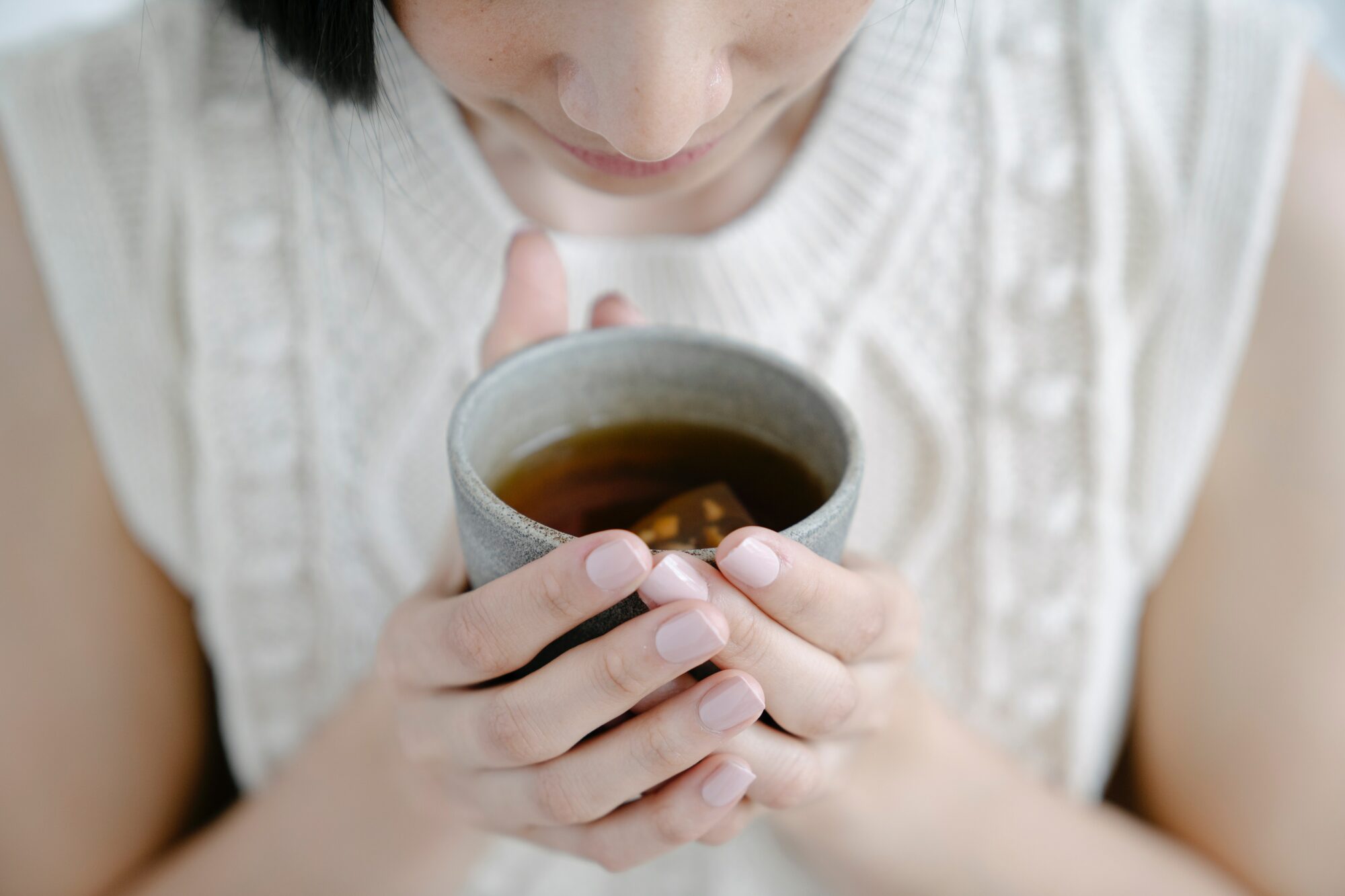 Woman in a white sleavless sweater holding a cup of tea - Is It Possible to Drink Too Much Tea?