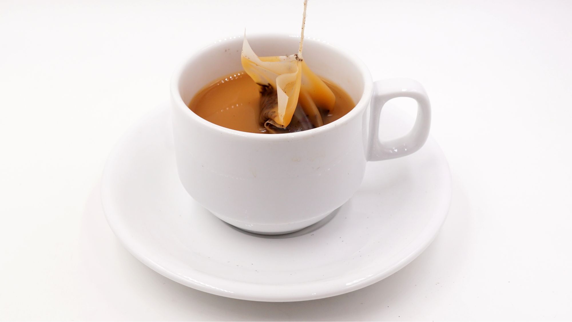 A white cup on a white background with a tea bag brewing inside - What Makes Tea Bitter?