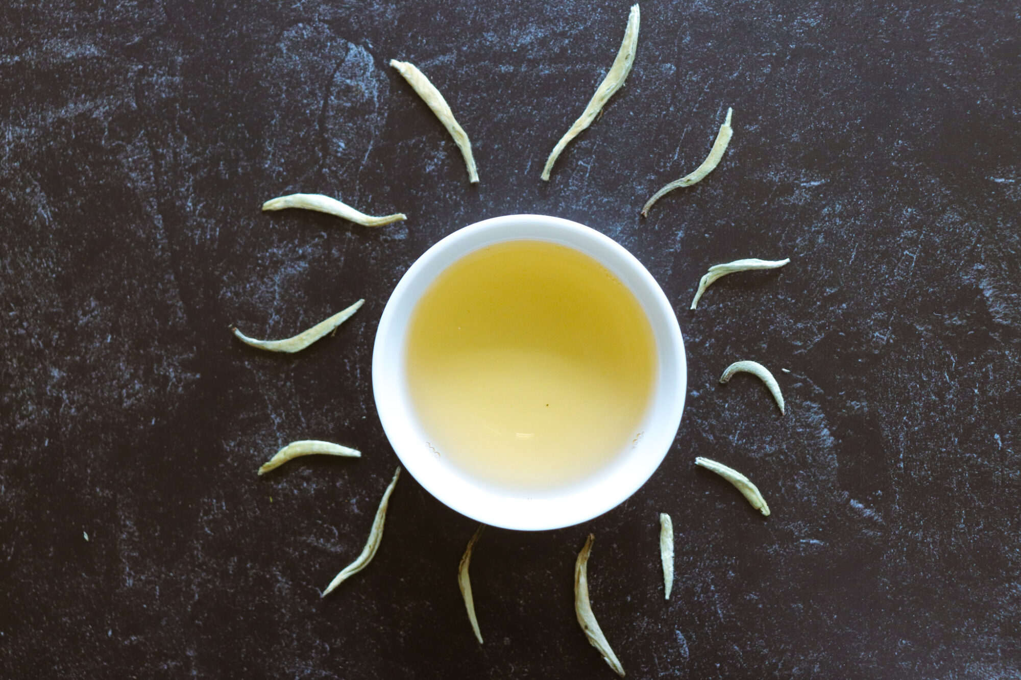 Art of Tea Organic Silver Needle White Tea &ndash; leaves around a cup of brewed tea